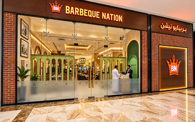 Silicon Central Mall featuring the Barbeque Nation restaurant storefront with glowing signage, glass entrance, warm lighting, and elegant marble flooring.